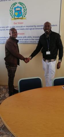 Mr Mudau from Chipa-Tabane Secondary School shakes hands with Mr Nyoni behind a board with the school vision and mission and the school badge above them.